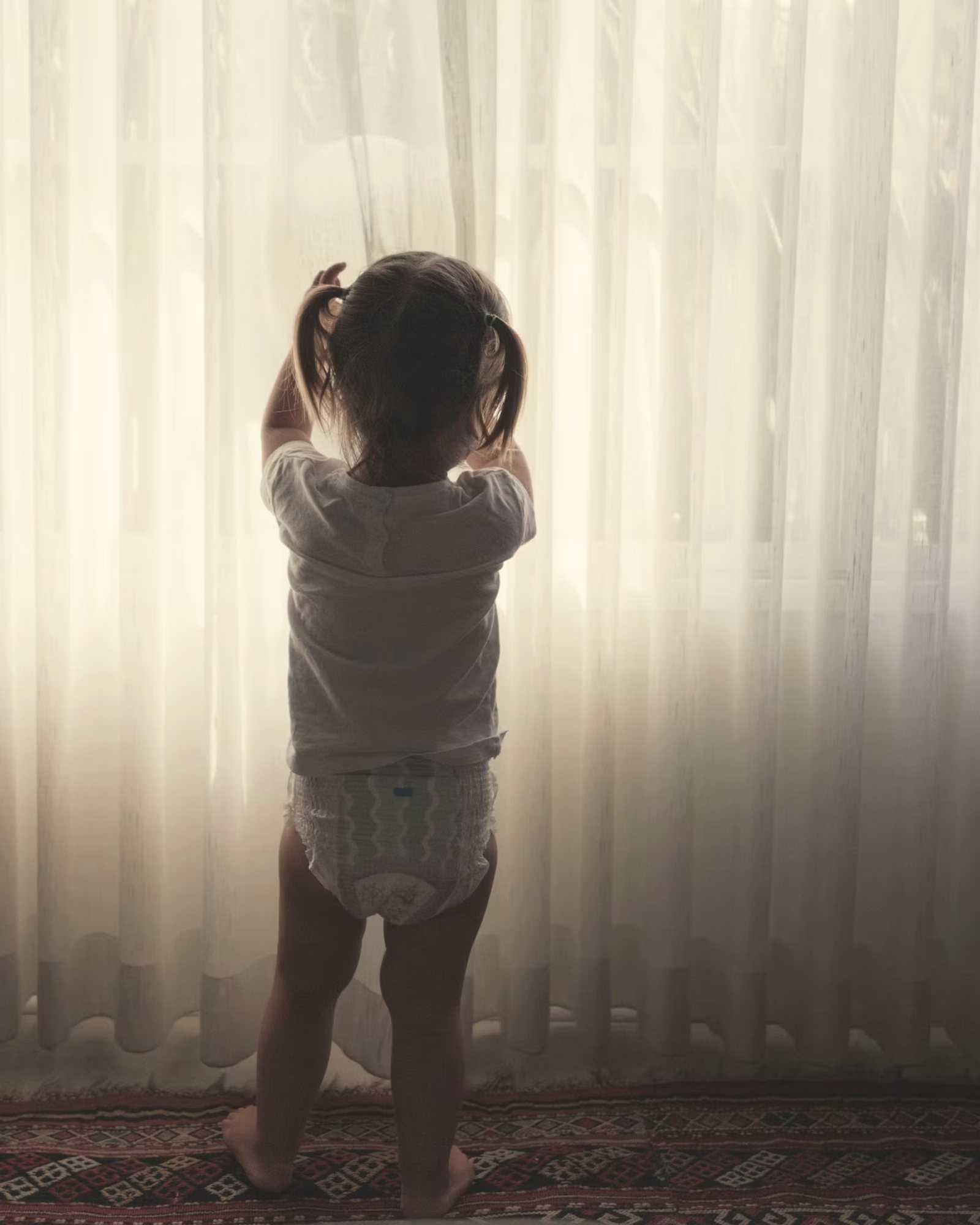 A child at a bright linen-curtained window.